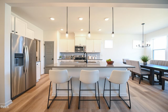 kitchen featuring decorative light fixtures, white cabinetry, sink, stainless steel appliances, and a center island with sink