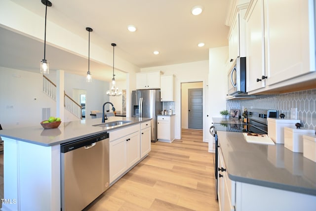 kitchen featuring sink, white cabinetry, hanging light fixtures, stainless steel appliances, and an island with sink