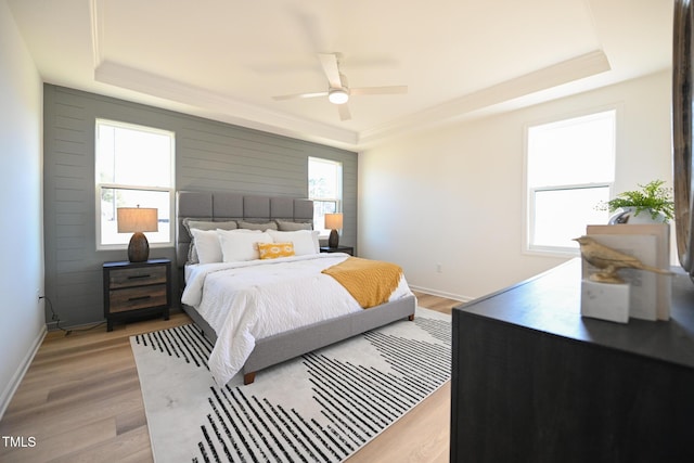 bedroom with ceiling fan, a tray ceiling, and light hardwood / wood-style floors