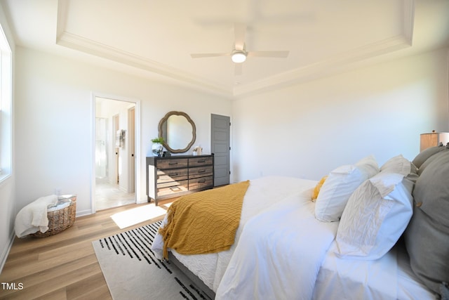 bedroom with ensuite bathroom, light hardwood / wood-style flooring, ceiling fan, and a tray ceiling