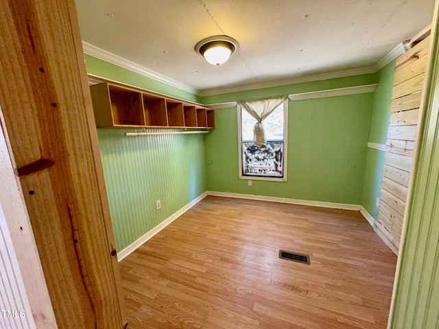 empty room with light hardwood / wood-style floors, ornamental molding, and wooden walls