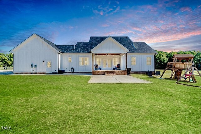 back of property at dusk with a lawn, board and batten siding, a playground, and a patio area