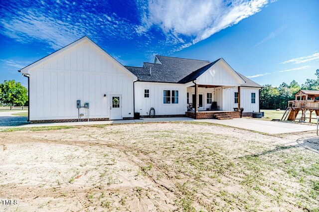 rear view of property with board and batten siding, a shingled roof, and a patio