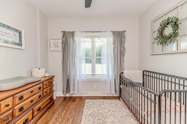 bedroom with light wood finished floors, baseboards, a crib, and ceiling fan