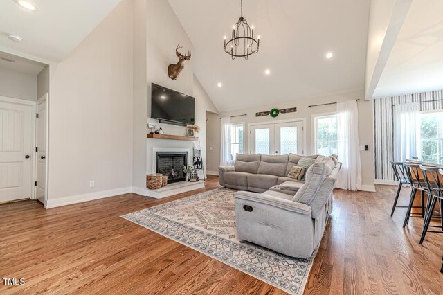 living area with high vaulted ceiling, wood finished floors, a chandelier, and a fireplace with raised hearth