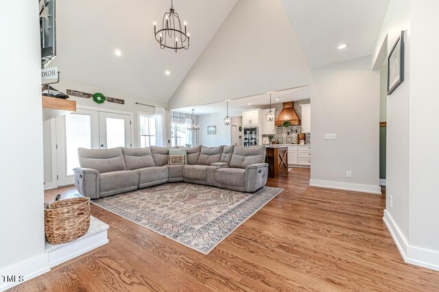 living area featuring baseboards, light wood-type flooring, high vaulted ceiling, and an inviting chandelier