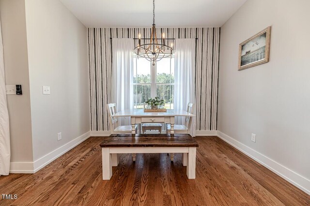 unfurnished dining area featuring a notable chandelier, baseboards, and wood finished floors