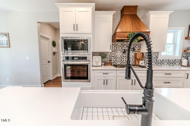 kitchen with decorative backsplash, light countertops, custom exhaust hood, stainless steel appliances, and white cabinetry