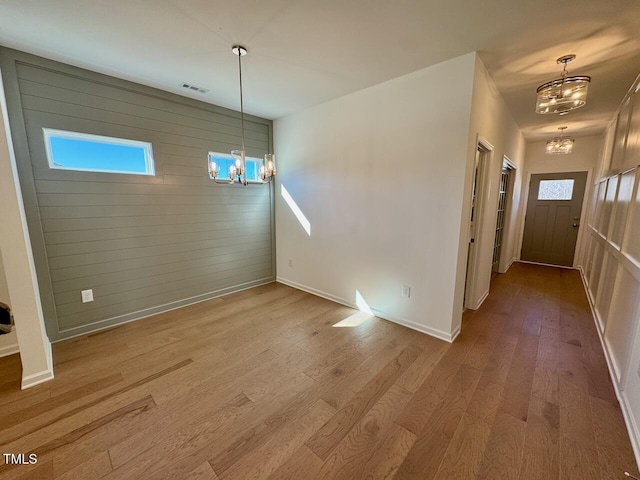 foyer with a chandelier, wooden walls, wood finished floors, visible vents, and baseboards