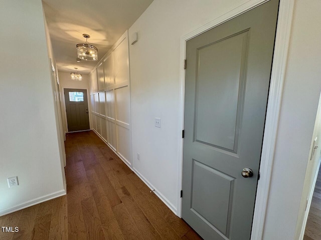 corridor featuring dark wood-style floors, baseboards, and a notable chandelier