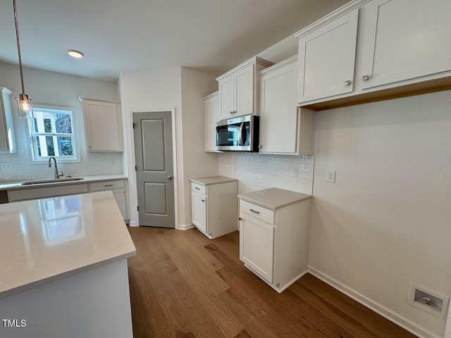 kitchen featuring dark wood-style flooring, a sink, white cabinetry, baseboards, and stainless steel microwave