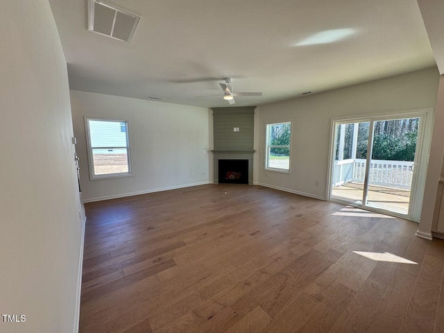 unfurnished living room with a ceiling fan, a large fireplace, visible vents, and wood finished floors