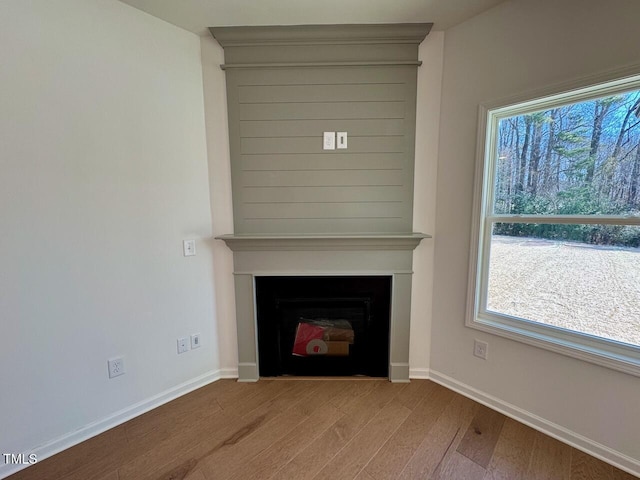 unfurnished living room with a large fireplace, baseboards, and wood finished floors