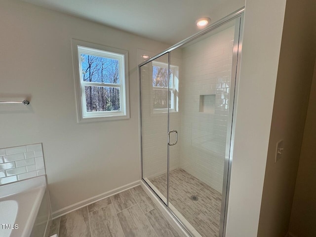 full bath featuring a stall shower, a bathtub, and baseboards