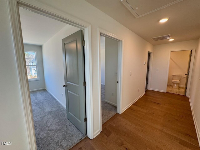 hallway featuring baseboards, wood finished floors, visible vents, and attic access