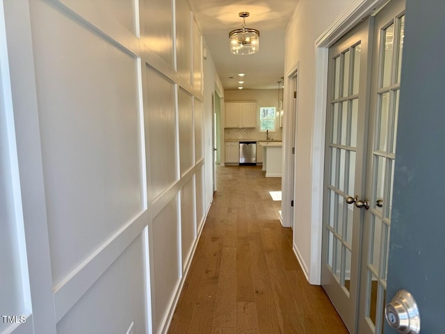 corridor with wood-type flooring, sink, a notable chandelier, and french doors