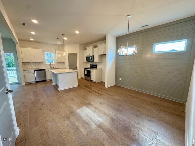 kitchen with visible vents, appliances with stainless steel finishes, white cabinets, wood finished floors, and a chandelier