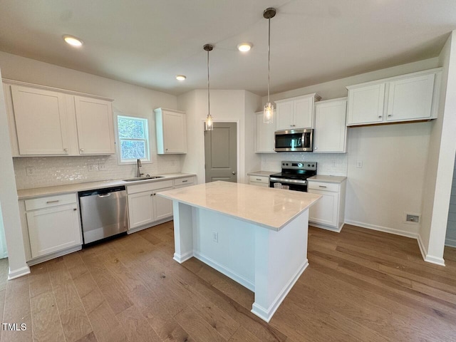 kitchen with stainless steel appliances, a sink, white cabinets, light countertops, and a center island