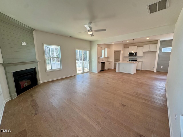 unfurnished living room featuring a fireplace, visible vents, baseboards, a ceiling fan, and light wood-type flooring