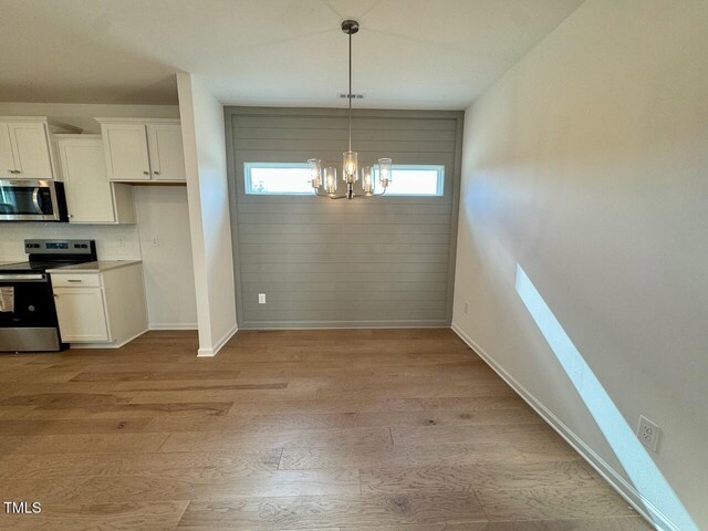 unfurnished dining area with light wood finished floors, baseboards, and an inviting chandelier