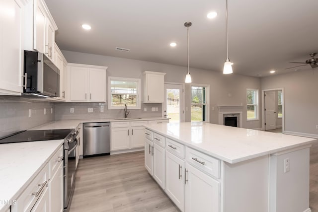 kitchen featuring a center island, sink, white cabinetry, stainless steel appliances, and light stone counters