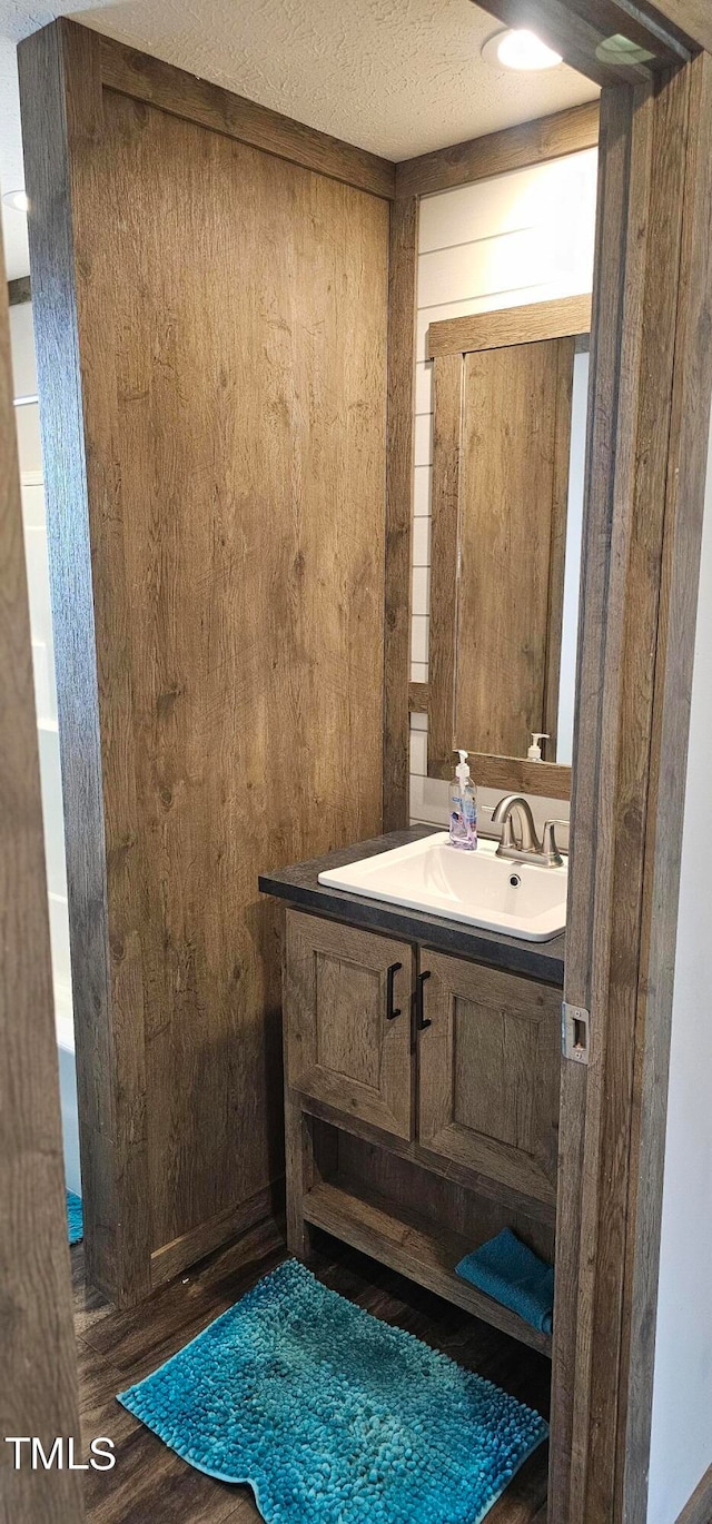 bathroom with a textured ceiling, vanity, wood walls, and wood-type flooring