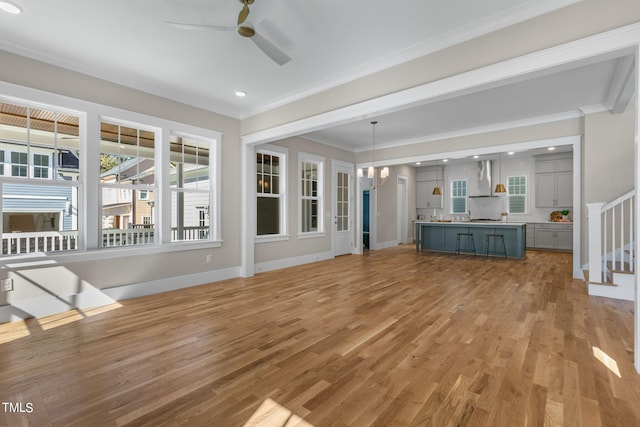 unfurnished living room with light hardwood / wood-style floors, crown molding, and ceiling fan with notable chandelier