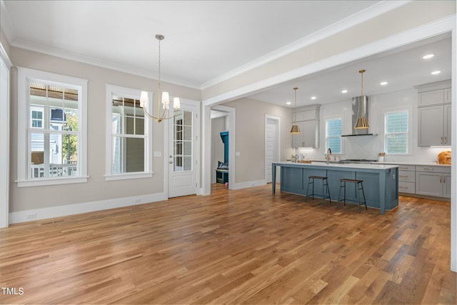 kitchen featuring a kitchen island, wall chimney range hood, a breakfast bar area, hanging light fixtures, and light wood-type flooring