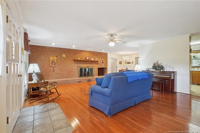 living room featuring brick wall, hardwood / wood-style floors, ceiling fan with notable chandelier, and a fireplace