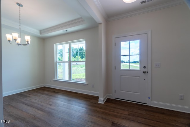 foyer entrance with dark wood-type flooring, a raised ceiling, an inviting chandelier, and ornamental molding