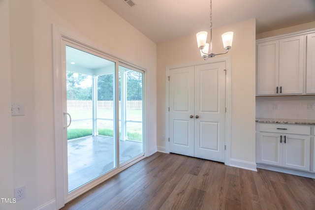 unfurnished dining area with visible vents, a notable chandelier, baseboards, and wood finished floors