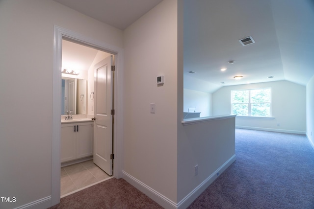 hall with vaulted ceiling, baseboards, light colored carpet, and visible vents