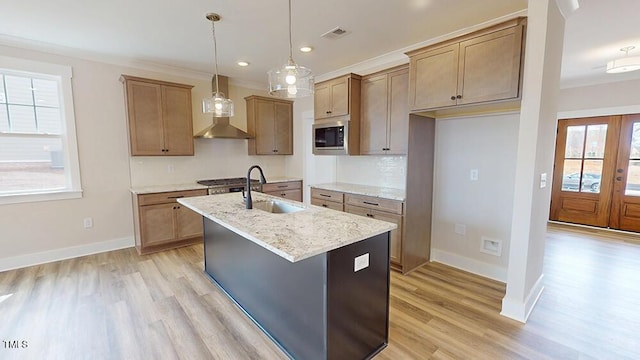 kitchen featuring visible vents, a center island with sink, light wood finished floors, stainless steel microwave, and wall chimney range hood