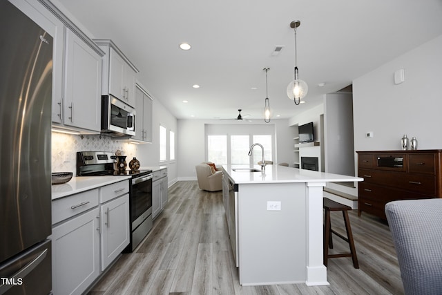 kitchen featuring an island with sink, pendant lighting, stainless steel appliances, light wood-type flooring, and sink