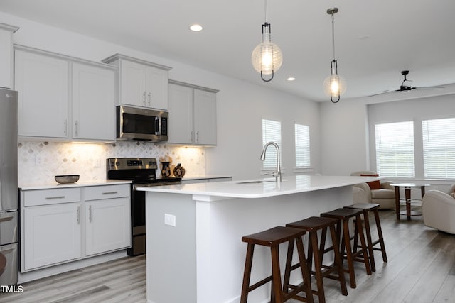 kitchen featuring ceiling fan, an island with sink, stainless steel appliances, and light wood-type flooring