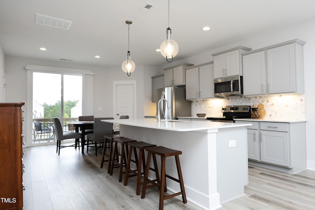 kitchen with pendant lighting, an island with sink, stainless steel appliances, and light wood-type flooring