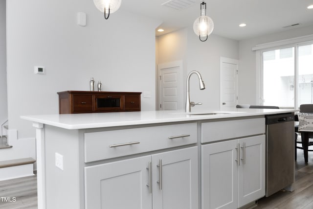 kitchen with light wood-type flooring, decorative light fixtures, stainless steel dishwasher, a kitchen island with sink, and sink