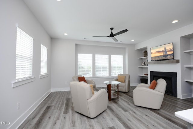 living room featuring ceiling fan, built in features, and light hardwood / wood-style flooring