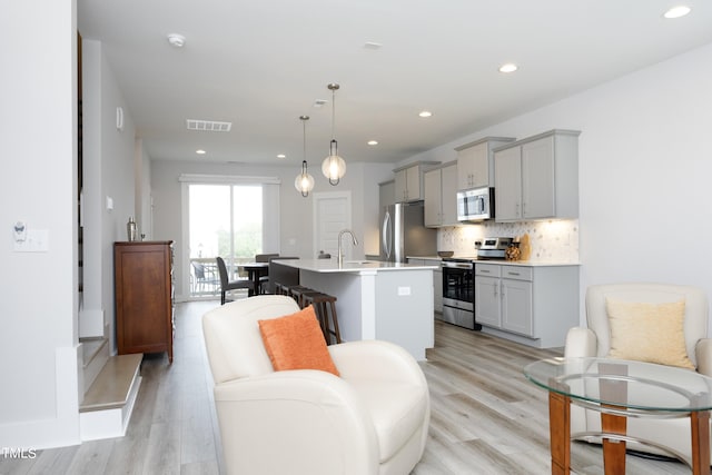 kitchen with appliances with stainless steel finishes, gray cabinetry, a kitchen island with sink, and pendant lighting