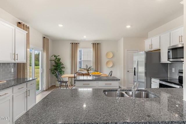 kitchen with a healthy amount of sunlight, stainless steel appliances, dark stone countertops, and white cabinetry