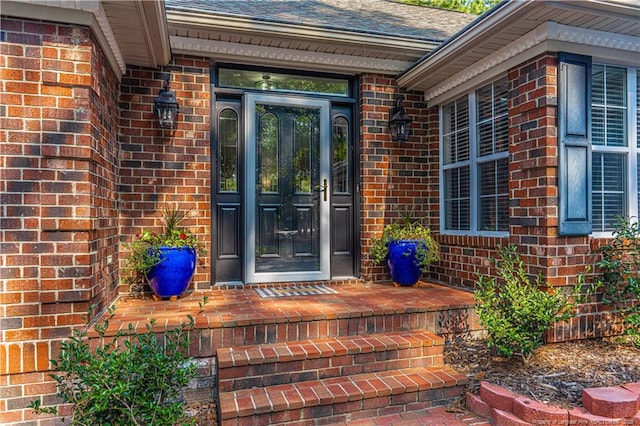 view of exterior entry with brick siding and roof with shingles