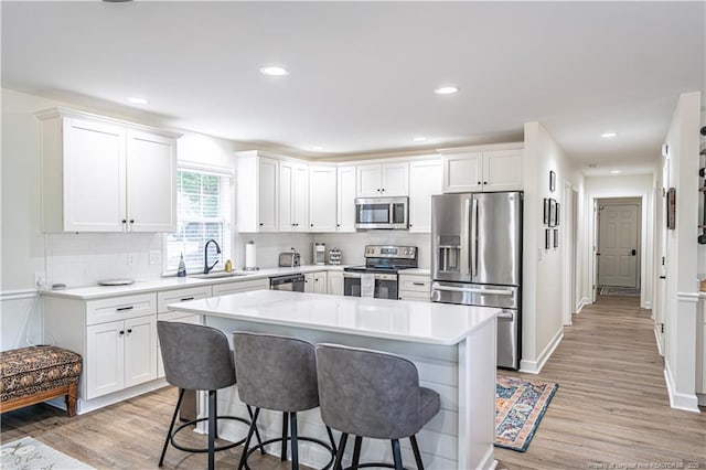 kitchen with a center island, a breakfast bar area, stainless steel appliances, light countertops, and white cabinets