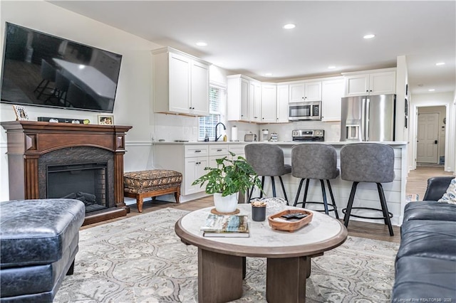 living area with recessed lighting, a fireplace with raised hearth, and light wood finished floors