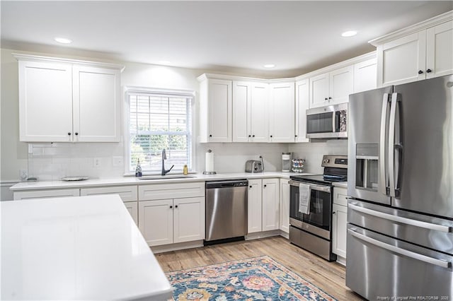 kitchen with white cabinets, stainless steel appliances, light countertops, light wood-type flooring, and a sink