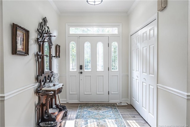 foyer entrance with ornamental molding and wood finished floors