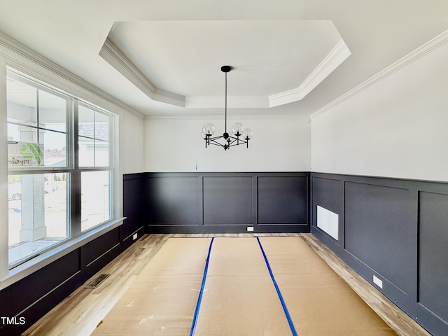 unfurnished dining area featuring a wainscoted wall, light wood finished floors, basketball hoop, a raised ceiling, and visible vents