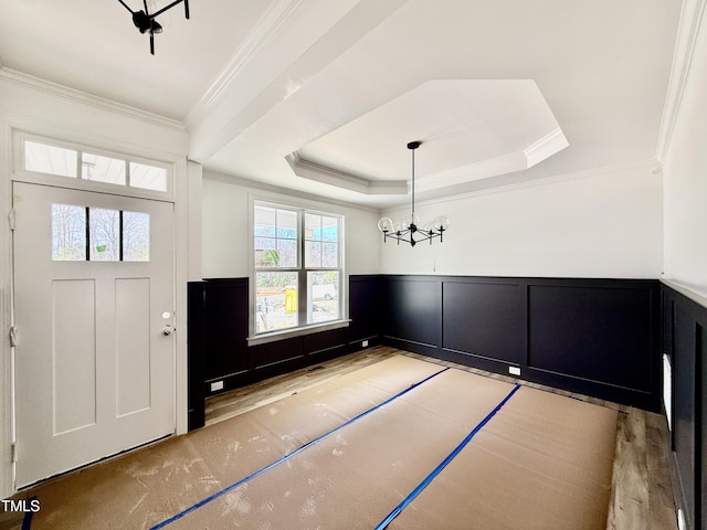 foyer entrance with a wainscoted wall, ornamental molding, a chandelier, and a tray ceiling