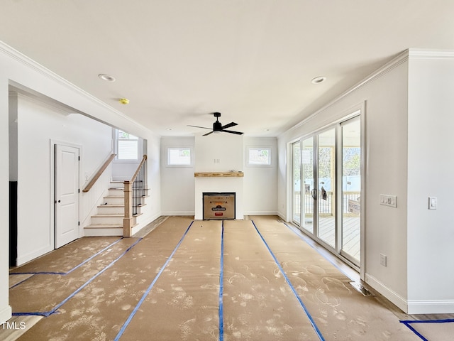 unfurnished living room with baseboards, ceiling fan, stairs, and crown molding