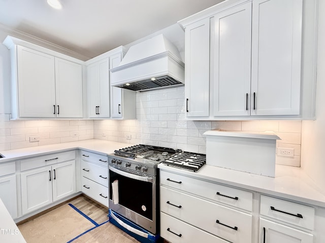 kitchen with custom range hood, decorative backsplash, white cabinetry, and stainless steel gas range