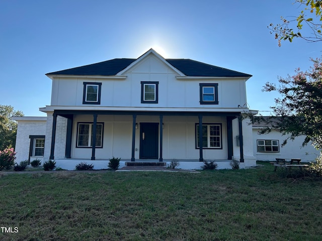 view of front of property with board and batten siding, a front lawn, brick siding, and covered porch